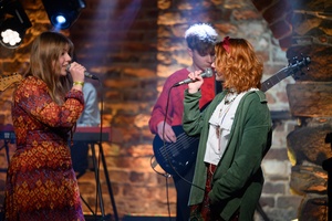 Koncert S.M.ROCK: na scenie dwie śpiewające uczennice i grający na gitarze basowej uczeń wykonujący piosenkę przed publicznością