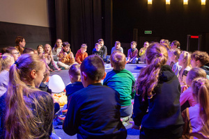 Filmowe ferie w kinie Marzenie - Na fotografii widzimy grupę dzieci siedzących w półkolu na scenie przed ekranem, podczas animacji poprzedzających projekcje filmowe w ramach cyklu "Filmowe ferie".