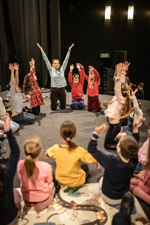 Filmowe ferie w kinie Marzenie - Na fotografii widzimy grupę dzieci siedzących w półkolu na scenie przed ekranem, podczas animacji poprzedzających projekcje filmowe w ramach cyklu "Filmowe ferie".