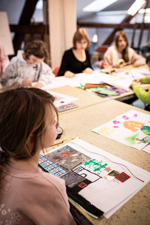 Artystyczne Ferie - tydzień I - Na zdjęciu przedstawione są dzieci uczestniczące w warsztatach plastycznych, skupione na malowaniu i rysowaniu. Widoczne są również osoby prowadzące, które instruują i inspirują młodych uczestników, zachęcając ich do twórczej ekspresji