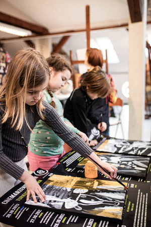 Artystyczne Ferie - tydzień I - Na zdjęciu przedstawione są dzieci uczestniczące w warsztatach plastycznych, skupione na malowaniu i rysowaniu. Widoczne są również osoby prowadzące, które instruują i inspirują młodych uczestników, zachęcając ich do twórczej ekspresji