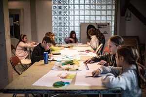 Artystyczne Ferie - tydzień I - Na zdjęciu przedstawione są dzieci uczestniczące w warsztatach plastycznych, skupione na malowaniu i rysowaniu. Widoczne są również osoby prowadzące, które instruują i inspirują młodych uczestników, zachęcając ich do twórczej ekspresji