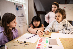 Artystyczne Ferie - tydzień I - Na zdjęciu przedstawione są dzieci uczestniczące w warsztatach plastycznych, skupione na malowaniu i rysowaniu. Widoczne są również osoby prowadzące, które instruują i inspirują młodych uczestników, zachęcając ich do twórczej ekspresji