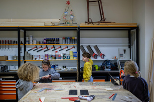 Naukowe Ferie w Pasażu Odkryć - Na zdjęciu przedstawieni są uczestnicy – dzieci i młodzież – zaangażowani w aktywności edukacyjne w różnych pracowniach naukowych, takich jak chemiczna, stolarska, planetarium oraz informatyczna. Widoczne są sceny, gdzie uczą się i przeprowadzają eksperymenty pod nadzorem instruktorów.