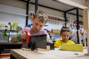 Naukowe Ferie w Pasażu Odkryć - Na zdjęciu przedstawieni są uczestnicy – dzieci i młodzież – zaangażowani w aktywności edukacyjne w różnych pracowniach naukowych, takich jak chemiczna, stolarska, planetarium oraz informatyczna. Widoczne są sceny, gdzie uczą się i przeprowadzają eksperymenty pod nadzorem instruktorów.
