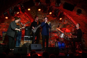 Koncert jazzowy: Tomasz Chyła Quintet - Zdjęcie sceny z koncertu Tomasz Chyła Quintet, pokazujące zaangażowanych muzyków. Tomasz Chyła gra na skrzypcach, w tle pozostali muzycy na różnych instrumentach. Scena jest dynamicznie oświetlona, co dodaje energii występowi.