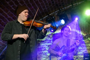 Koncert jazzowy: Tomasz Chyła Quintet - Zdjęcie sceny z koncertu Tomasz Chyła Quintet, pokazujące zaangażowanych muzyków. Tomasz Chyła gra na skrzypcach, w tle pozostali muzycy na różnych instrumentach. Scena jest dynamicznie oświetlona, co dodaje energii występowi.