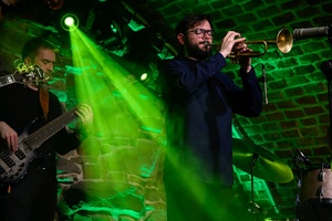 Koncert jazzowy: Tomasz Chyła Quintet - Zdjęcie sceny z koncertu Tomasz Chyła Quintet, pokazujące zaangażowanych muzyków. Tomasz Chyła gra na skrzypcach, w tle pozostali muzycy na różnych instrumentach. Scena jest dynamicznie oświetlona, co dodaje energii występowi.