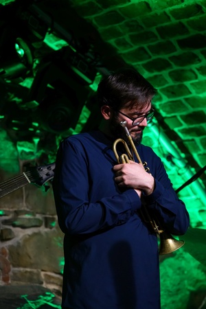 Koncert jazzowy: Tomasz Chyła Quintet - Zdjęcie sceny z koncertu Tomasz Chyła Quintet, pokazujące zaangażowanych muzyków. Tomasz Chyła gra na skrzypcach, w tle pozostali muzycy na różnych instrumentach. Scena jest dynamicznie oświetlona, co dodaje energii występowi.