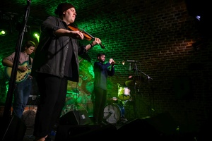 Koncert jazzowy: Tomasz Chyła Quintet - Zdjęcie sceny z koncertu Tomasz Chyła Quintet, pokazujące zaangażowanych muzyków. Tomasz Chyła gra na skrzypcach, w tle pozostali muzycy na różnych instrumentach. Scena jest dynamicznie oświetlona, co dodaje energii występowi.