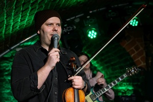 Koncert jazzowy: Tomasz Chyła Quintet - Zdjęcie sceny z koncertu Tomasz Chyła Quintet, pokazujące zaangażowanych muzyków. Tomasz Chyła gra na skrzypcach, w tle pozostali muzycy na różnych instrumentach. Scena jest dynamicznie oświetlona, co dodaje energii występowi.