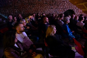 Koncert jazzowy: Tomasz Chyła Quintet - Zdjęcie sceny z koncertu Tomasz Chyła Quintet, pokazujące zaangażowanych muzyków. Tomasz Chyła gra na skrzypcach, w tle pozostali muzycy na różnych instrumentach. Scena jest dynamicznie oświetlona, co dodaje energii występowi.