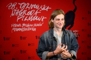 38. TNF - Dzień 3 (2.06.2024) - Odtwórca jednej z głównych ról w filmie "Kobieta z..." Mateusz Więcławek na tle ścianki festiwalowej w holu Marzenia