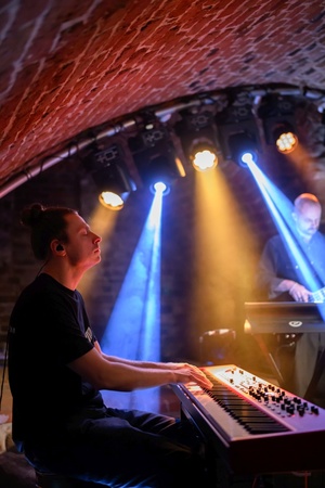 Koncert: Ania Szlagowska - Muzycy grający na instrumentach podczas koncertu na oświetlonej scenie.