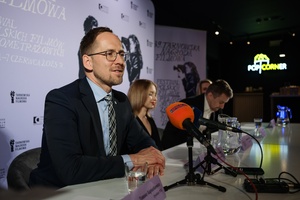 39 TNF: Konferencja prasowa - Na pierwszym planie prezydent Tarnowa Jakub Kwaśny zza stołu konferencyjnego witający dziennikarzy na spotkaniu