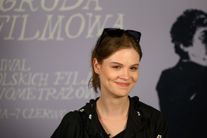 39. TNF: Dzień 3 (1.06.2025) - Aktorka Matylda Giegżno w oczekiwaniu na spotkanie z publicznością po projekcji filmu "Światłoczuła" na tle ścianki 39. TNF w hallu kina