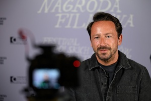 39. TNF: Dzień 3 (1.06.2025) - Reżyser Tadeusz Śliwa w oczekiwaniu na spotkanie z publicznością po projekcji filmu "Światłoczuła" na tle ścianki 39. TNF w hallu kina