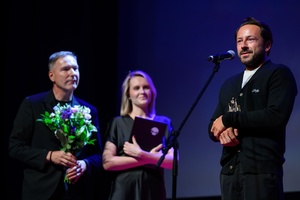 39. TNF: Gala Wręczenia Nagród (7.06.2025) - Na scenie Tadeuszowi Śliwie reżyser "Światłoczułej" przemawiający do widzów, w tle dyr. TCK Tomasz Kapturkiewicz i jego zastępczyni Dominika Dąbek