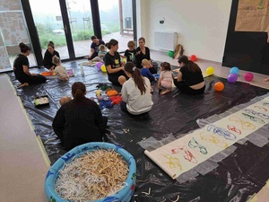 Warsztaty sensoplastyczne - Uczestnicy warsztatów wraz z opiekunami na sali warsztatowej, na pierwszym planie basen ze ściankami papieru i folia bąbelkowa