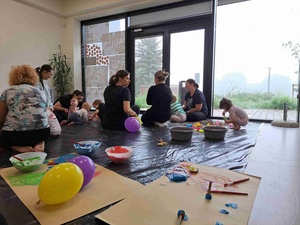 Warsztaty sensoplastyczne - Uczestnicy warsztatów wraz z opiekunami na sali warsztatowej, na pierwszym planie kartki papieru i balony