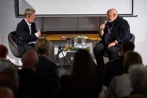 Wystawa: Zrozumie życie - Marek Grygiel i Tadeusz Koniarz siedzący na środku sali, w fotelach na podwyższeniu, w trakcie spotkania.